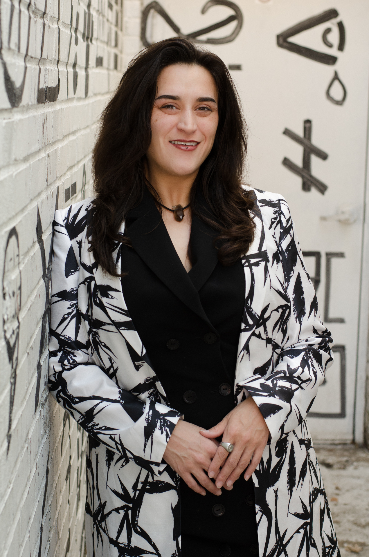 Lucinda Garcia, owner of Vesta Events, in a black and white patterned blazer against a painted brick wall